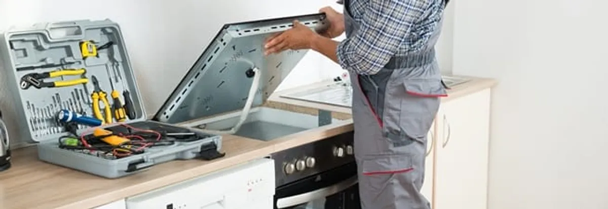 Cooktop repair technician lifting a built-in stovetop for service in Savannah, GA